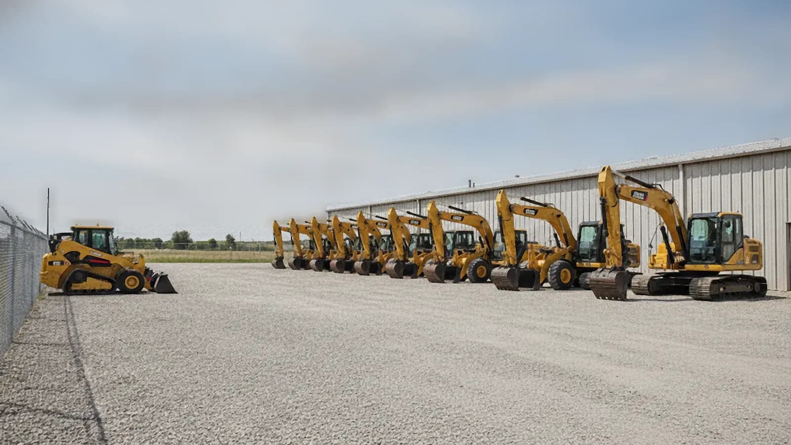 Rows of excavators and loaders parked in a tidy construction equipment rental yard on a sunny day